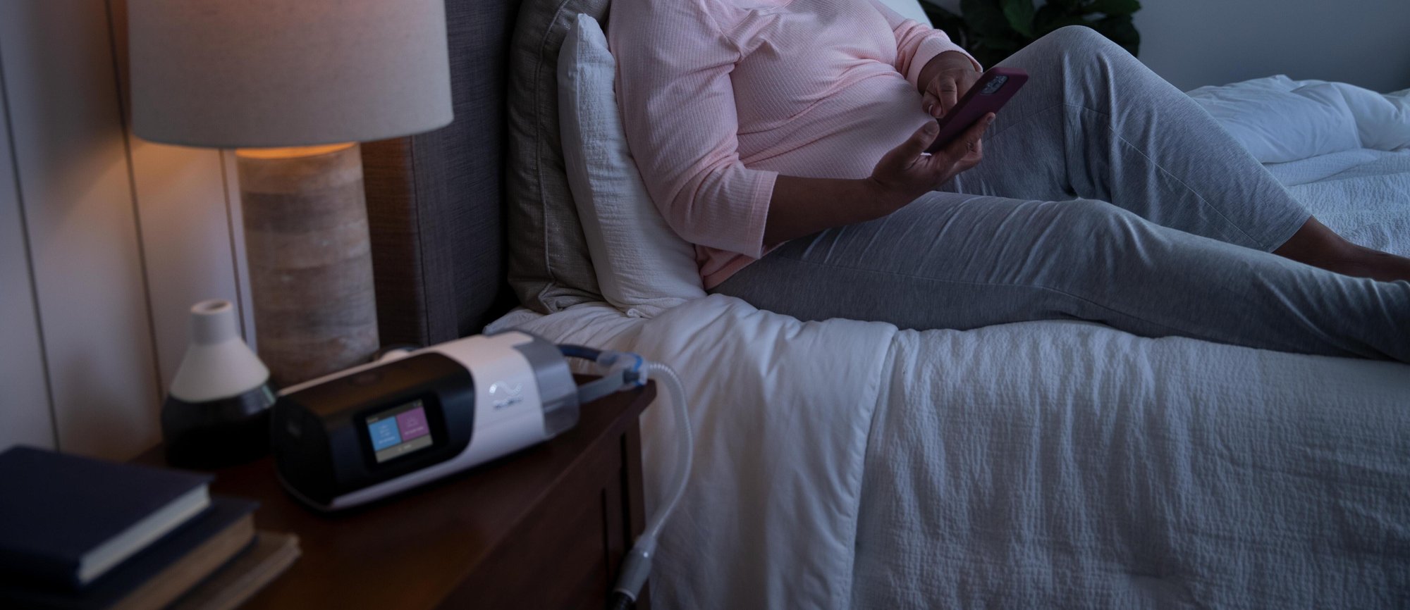 Woman on bed holding her phone, staying up late.