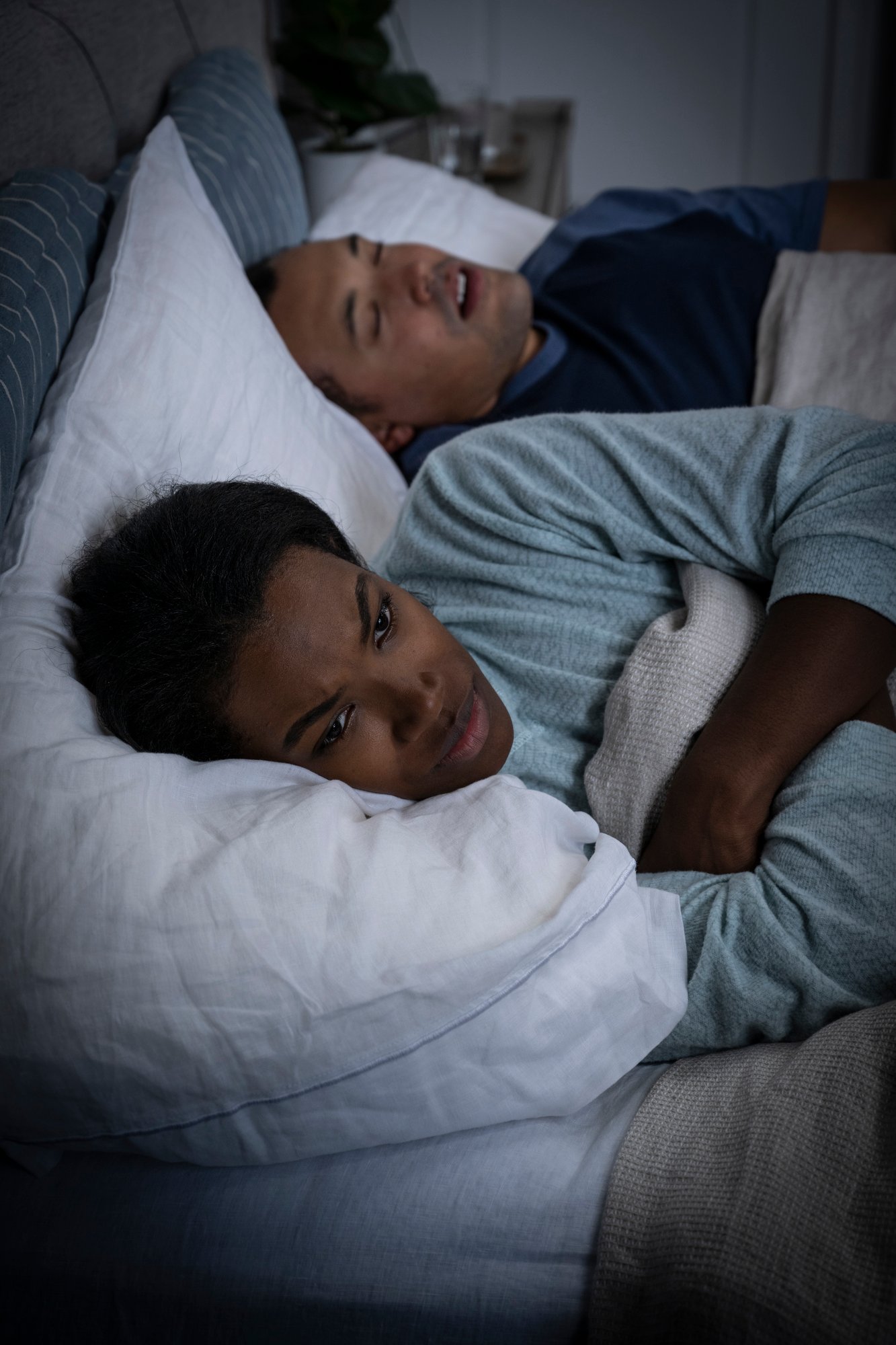 Man and woman in bed, man is snoring and the woman is awake looking upset