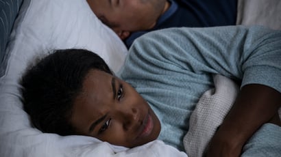 Man and woman in bed, man is snoring and the woman is awake looking upset