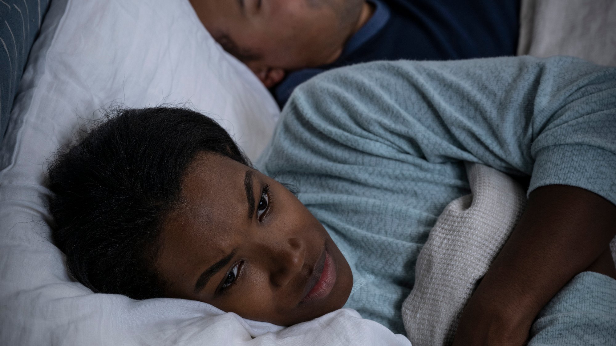 Man and woman in bed, man is snoring and the woman is awake looking upset