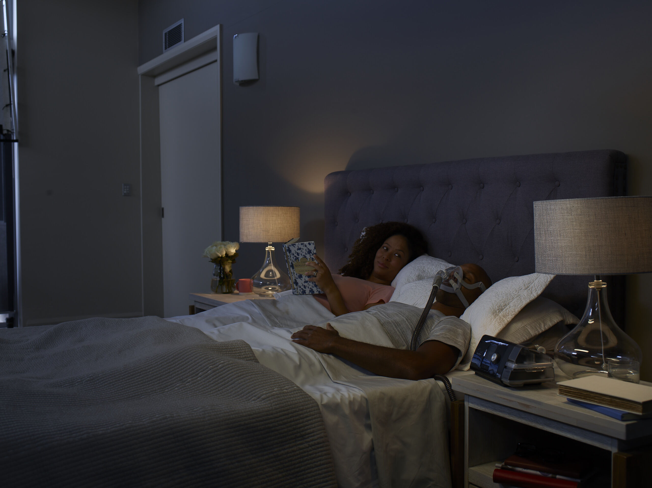 Woman stays up next to man in bed, it is night time.